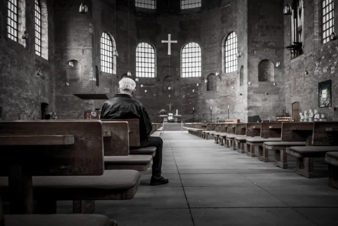Un uomo in preghiera davanti ad una croce in una chiesa | pxhere - public domain